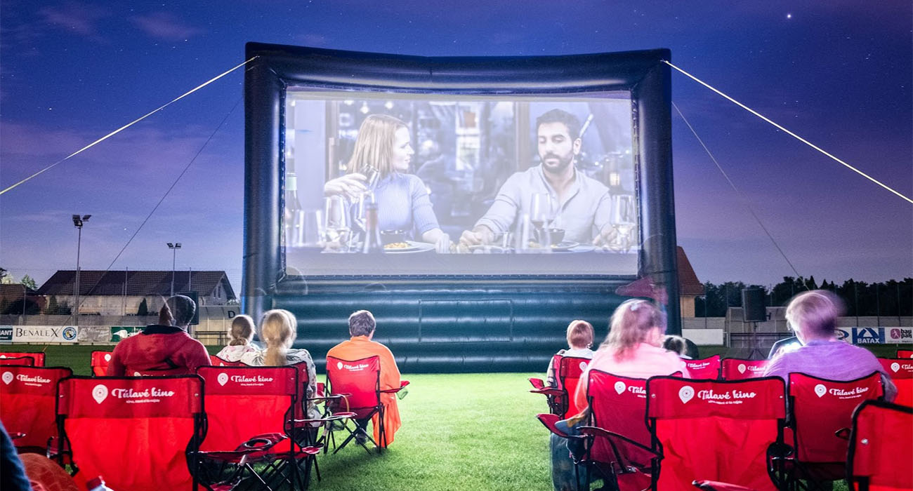 Ľudia si užívajú premietanie filmu na čerstvom vzduchu. Sedia na stoličkách s logom Túlavé kino.